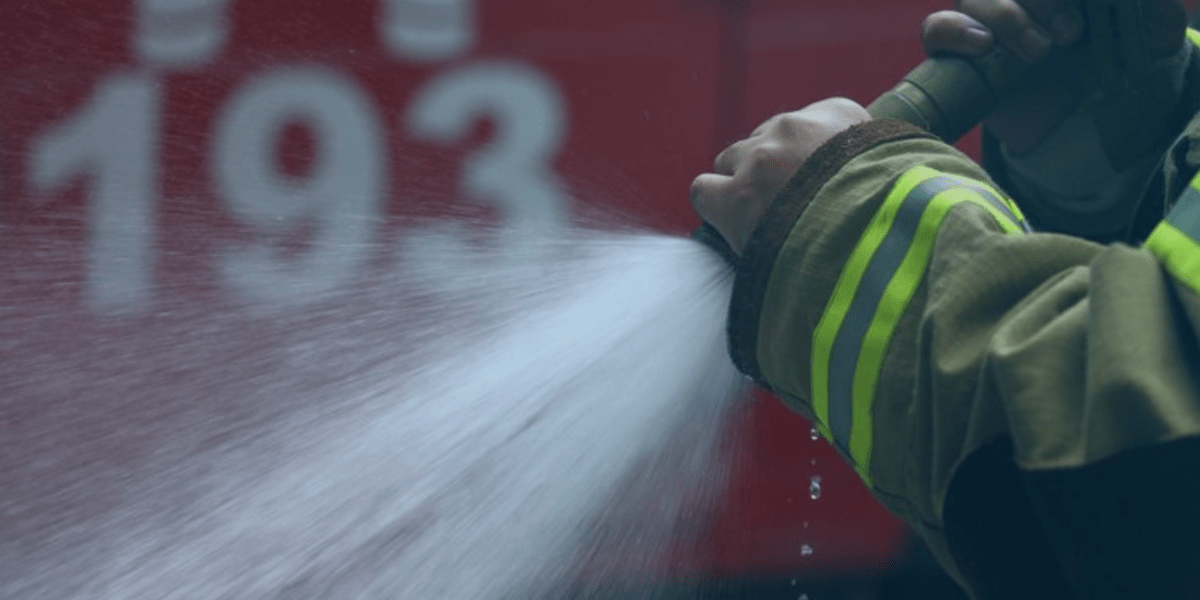 mão com uniforme do bombeiro controlando a saída do jato da mangueira de incêndio