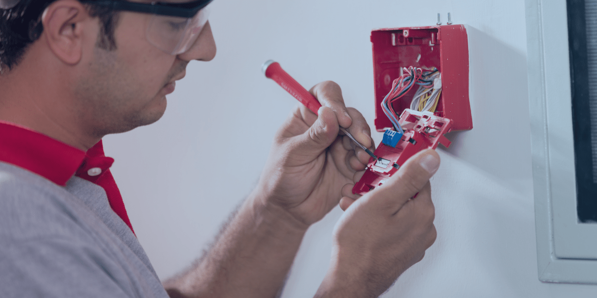 homem instalando os fios de conexão do acionador de alarme